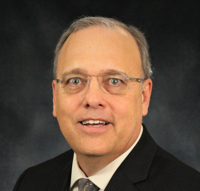 A person
                  wearing a suit and tie smiling at the camera
                  Description automatically generated